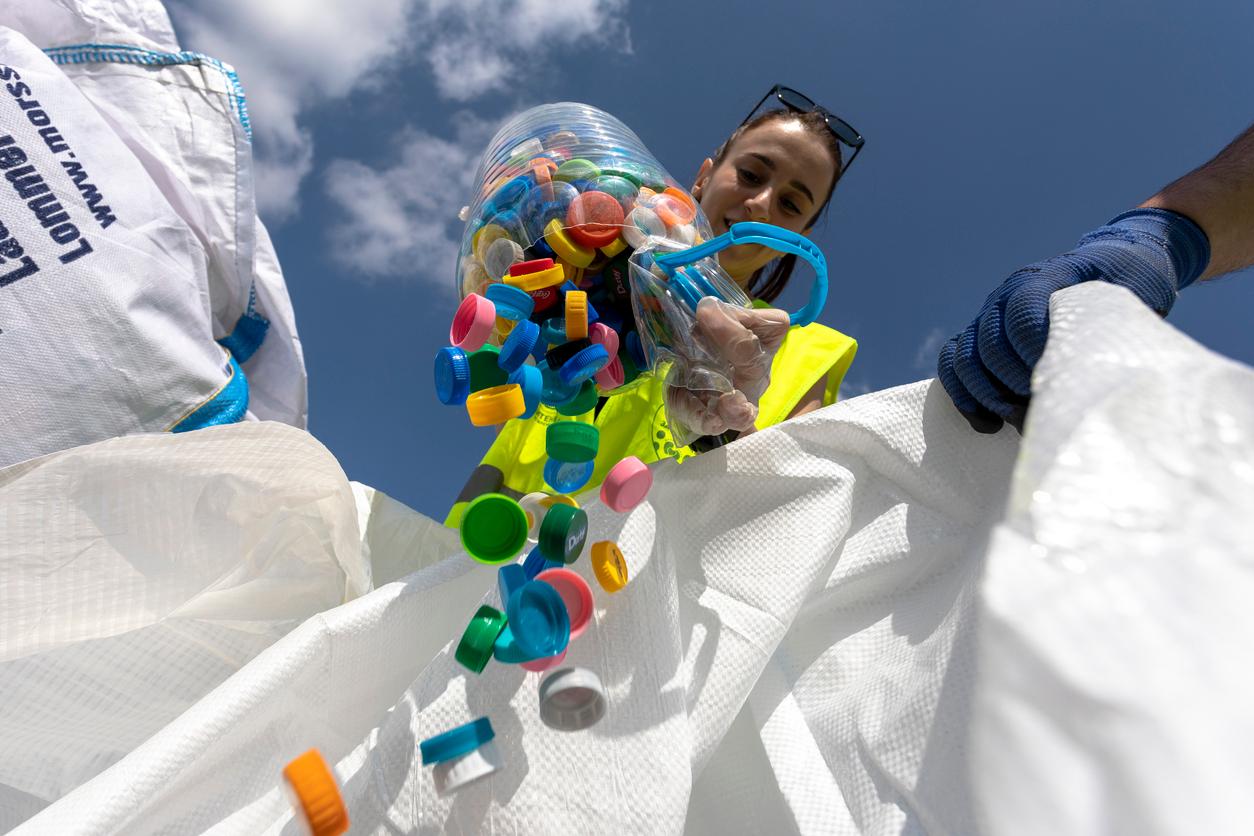 Person pouring a tub of colorful plastic bottle caps into a white bag.