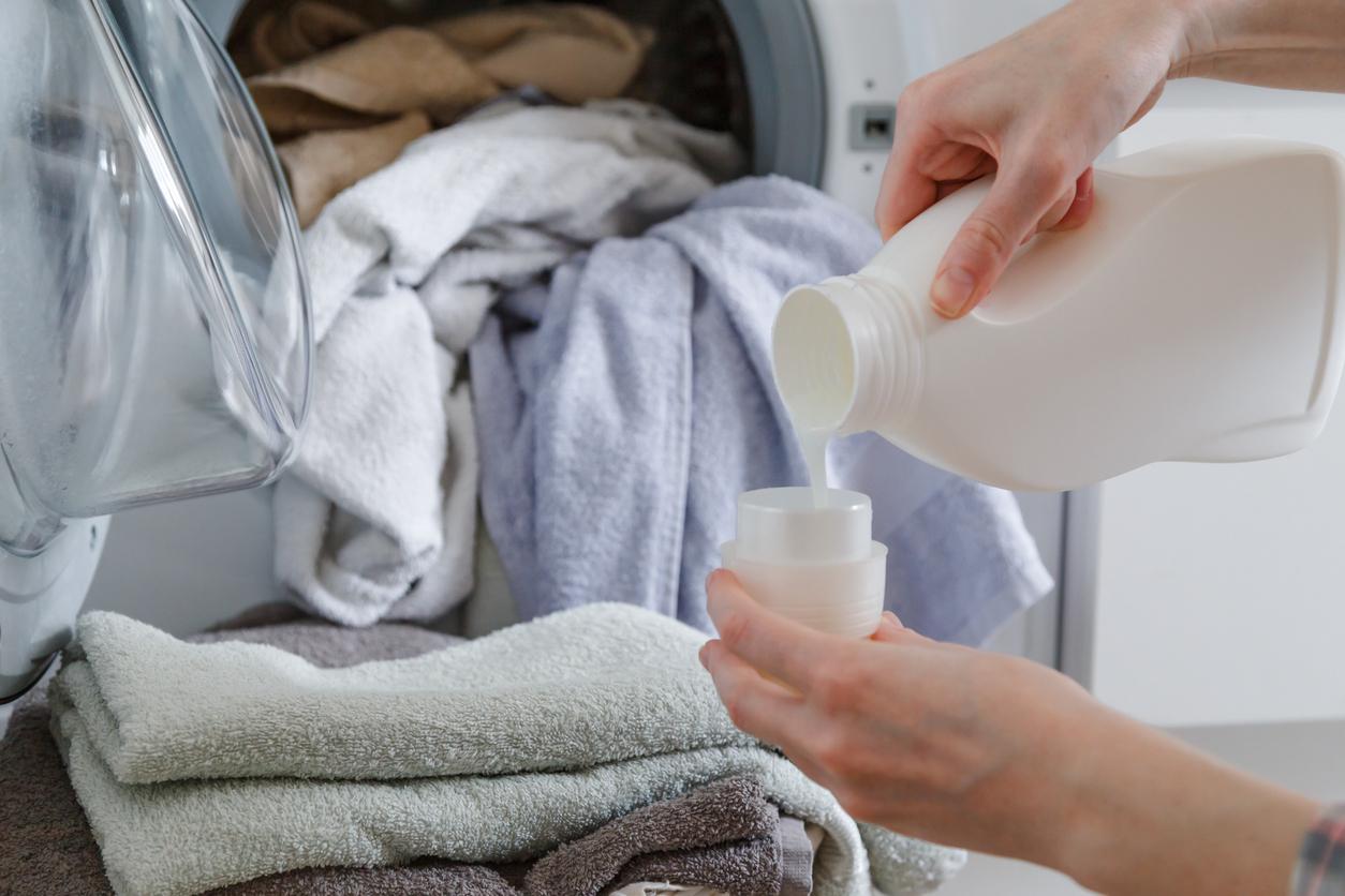 A person pours laundry soap into a cup in their laundry room.