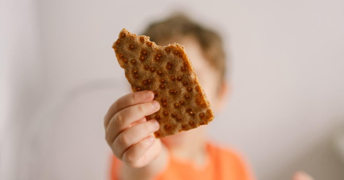 Little boy, out of focus, holds crispbread up in focus