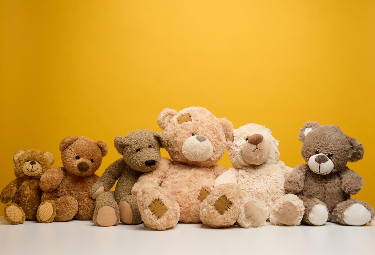 A group of teddy bears are pictured in a row in front of a yellow background,