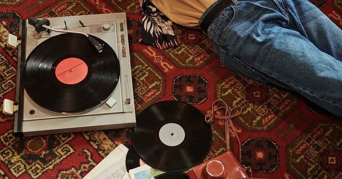 Photo of two black vinyl records and a record player on the floor next to a person laying down partially out of frame
